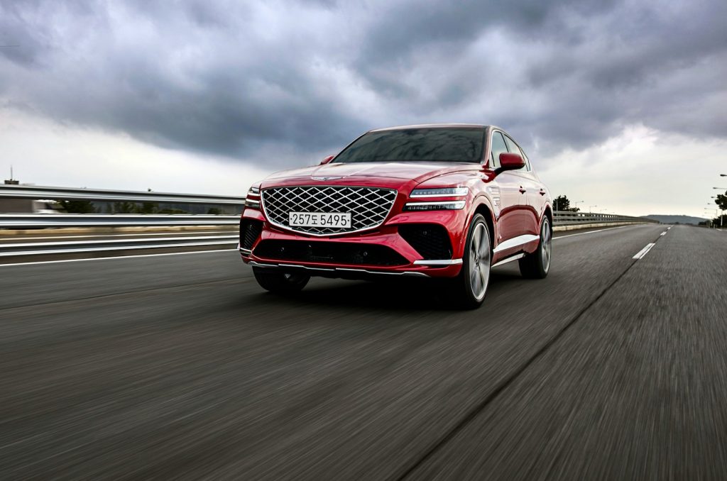 a red car driving down a road under a cloudy sky