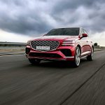 a red car driving down a road under a cloudy sky