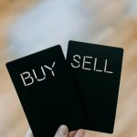 a hand holding two black cards with the words buy and sell written on them