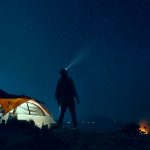 man standing beside camping tent wearing headlamp during nighttime